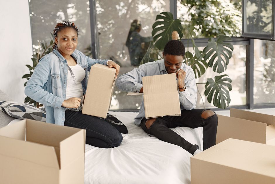 Two movers from Man with Van Leaves Green are engaged in the home relocation process, lifting a green upholstered sofa with a smooth fabric finish and wooden legs, positioning it through a clear doorw