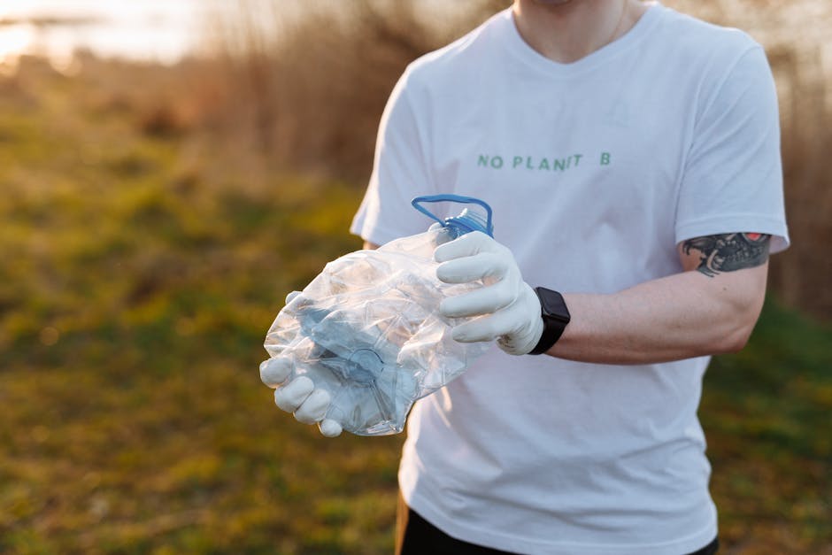 A man wearing a white t-shirt with the words 'NO PLANT B' printed on it, white gloves, and a black wristwatch is standing outdoors during daylight hours, holding a transparent plastic bag filled with crumpled paper or packing materials and a blue plastic drawstring closure. The background features blurred greenery and warm natural lighting, indicating a rural or suburban setting. The man appears to be involved in packing or preparing items, possibly as part of a home relocation or moving process, with his focus on handling packing materials. The scene suggests activities related to packing and moving, typical for house removals or furniture transport as coordinated by Man with Van Leaves Green, specializing in removals and relocation services.